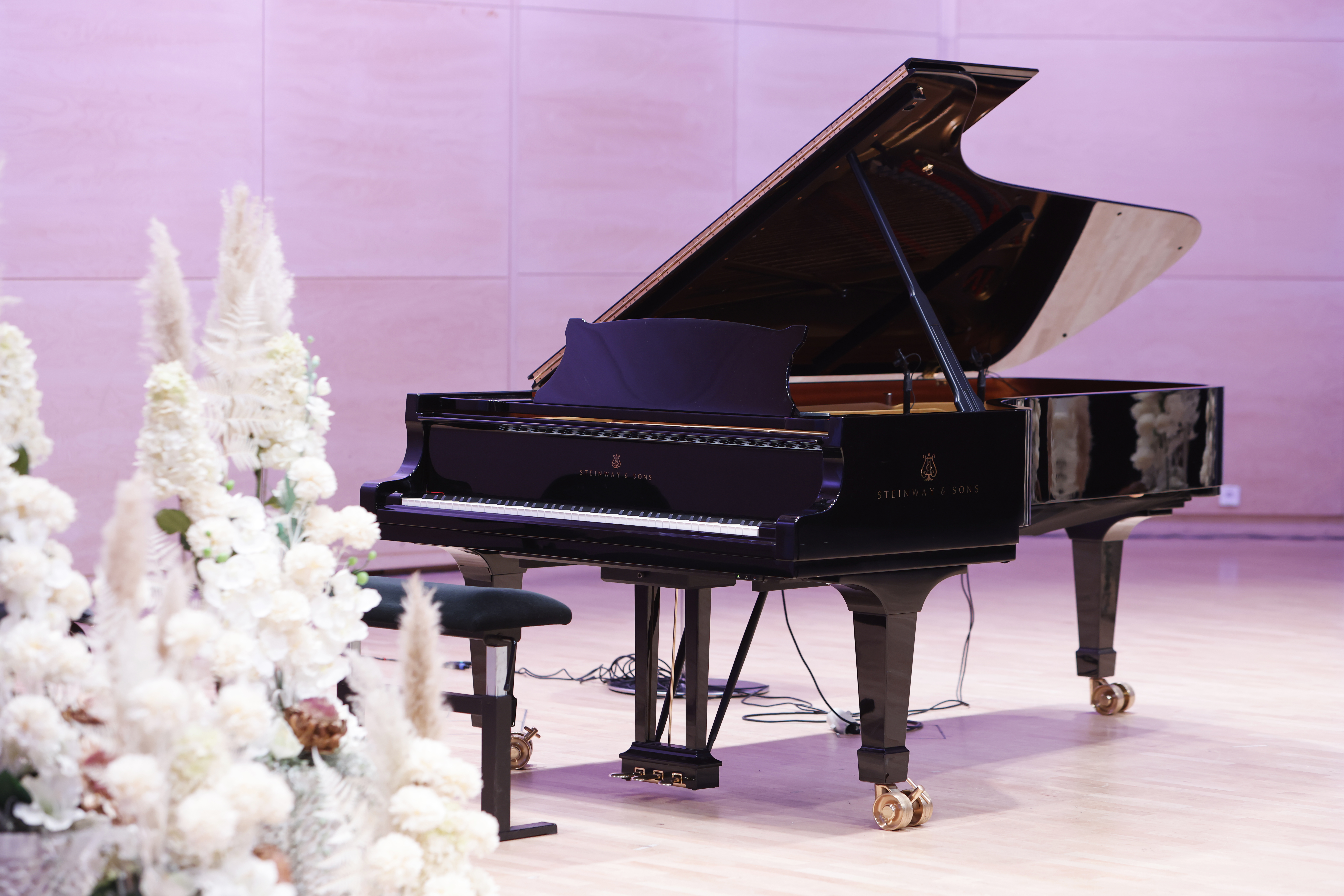 Piano lavalla pinkissä valaistuksessa, valkoisia kukkia edustalla.